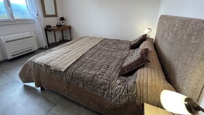 Een slaapkamer met een bed, een bedlampje, een raam, een radiator en een klein tafeltje met een lamp.