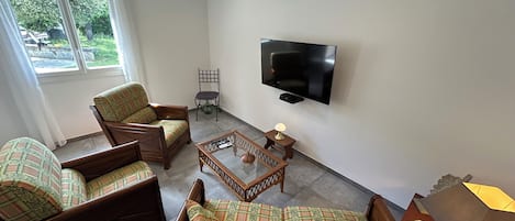 A living room with a flat-screen TV, two armchairs, a sofa, a coffee table, and a lamp.