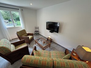 Ett vardagsrum med en platt-TV, två fåtöljer, en soffa, ett soffbord och en lampa.
