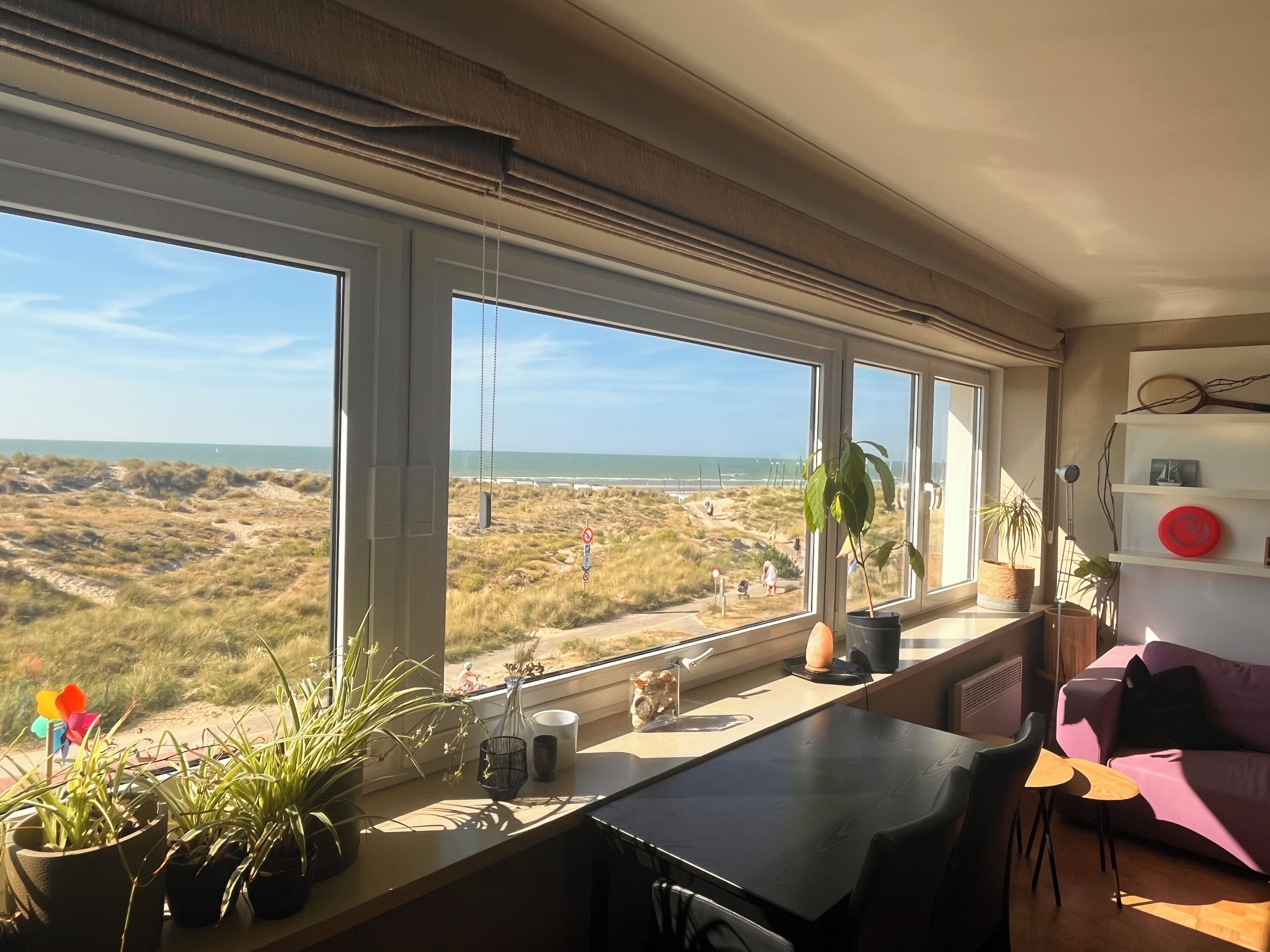 Une pièce dotée d’une grande fenêtre donnant sur une plage, d’une table avec des chaises et d’un canapé.