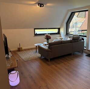 Una sala de estar moderna con un sofá, una mesita, un televisor y una ventana con vistas a edificios.