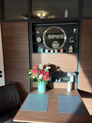 Una habitación con un escritorio de madera, un florero de flores, un reloj y una estantería con varios objetos.