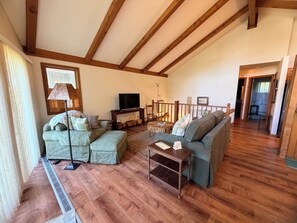 A cozy living room with wooden beams, a sofa set, a TV, and a dining area.