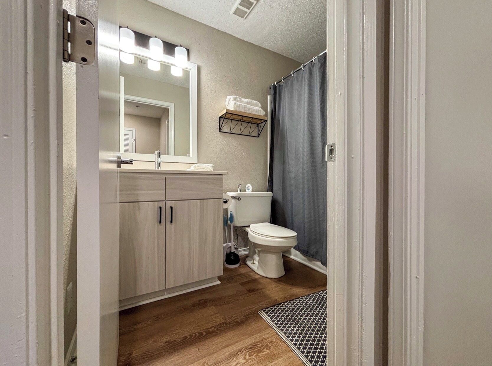 Un baño con tocador de madera, inodoro, cortina de ducha y espejo con luces.