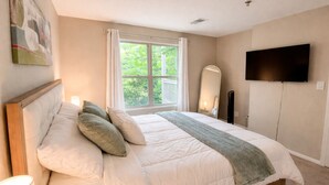 Ein Schlafzimmer mit einem großen Bett, einem an der Wand montierten Fernseher und einem Fenster mit Vorhängen.