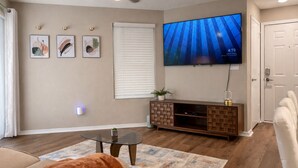 Ein Wohnzimmer mit Flachbildfernseher, einem Glastisch, einem braunen Sofa, einem gemusterten Teppich und einer Holz-Unterhaltungseinheit.