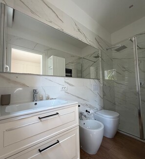 Un baño con salpicadero de mármol, un espejo grande, un lavabo, un inodoro y un bidé.