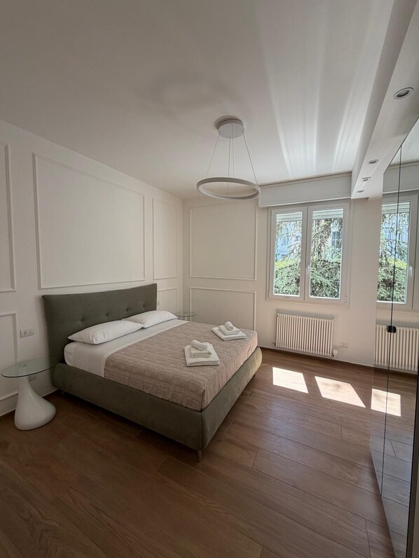 Ein Schlafzimmer mit Bett, Nachttisch, Pendelleuchte, Fenster und Heizkörper.