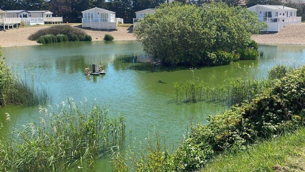 A lakeside area with mobile homes and a small boat. - This Caravan is no Longer Available (New Romney)