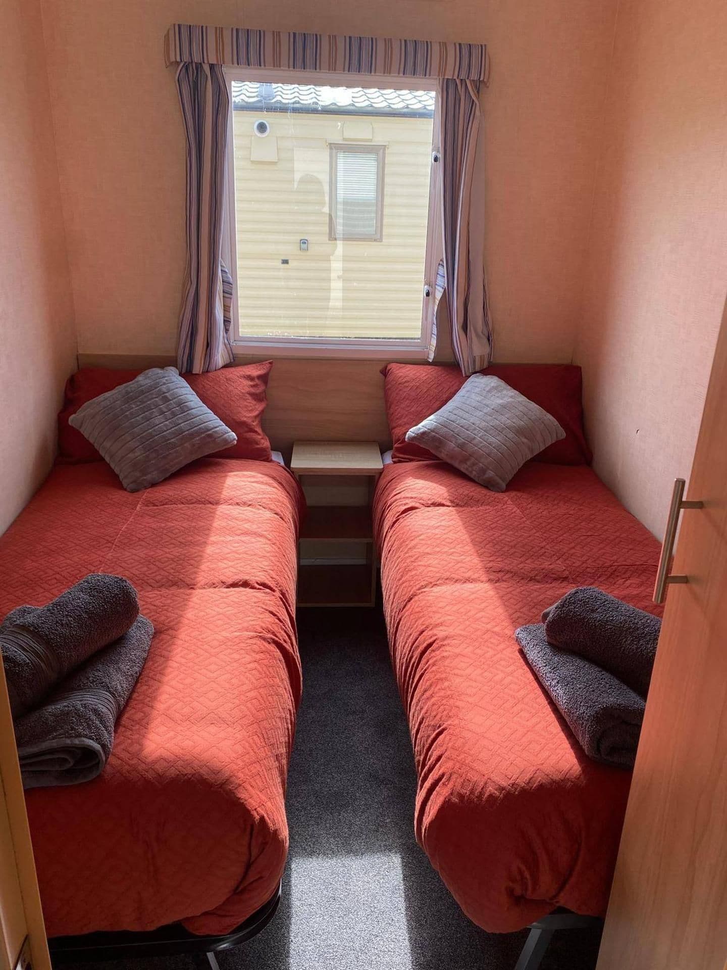 A compact room with two beds, each with a pillow and a rolled towel.