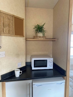 Una kitchenette con microondas, un refrigerador pequeño, una taza de café y una planta en maceta sobre una repisa.