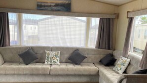 A caravan interior with a sofa, curtains, a ceiling light, and a window. - This Caravan is no Longer Available (New Romney)