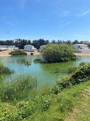 A lakeside view with mobile homes and a small boat. - This Caravan is no Longer Available (New Romney)