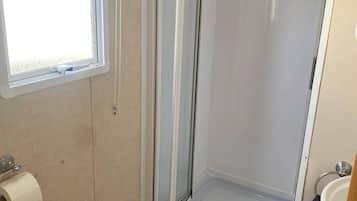 A small bathroom with a glass shower enclosure, a toilet, a sink, and a window.