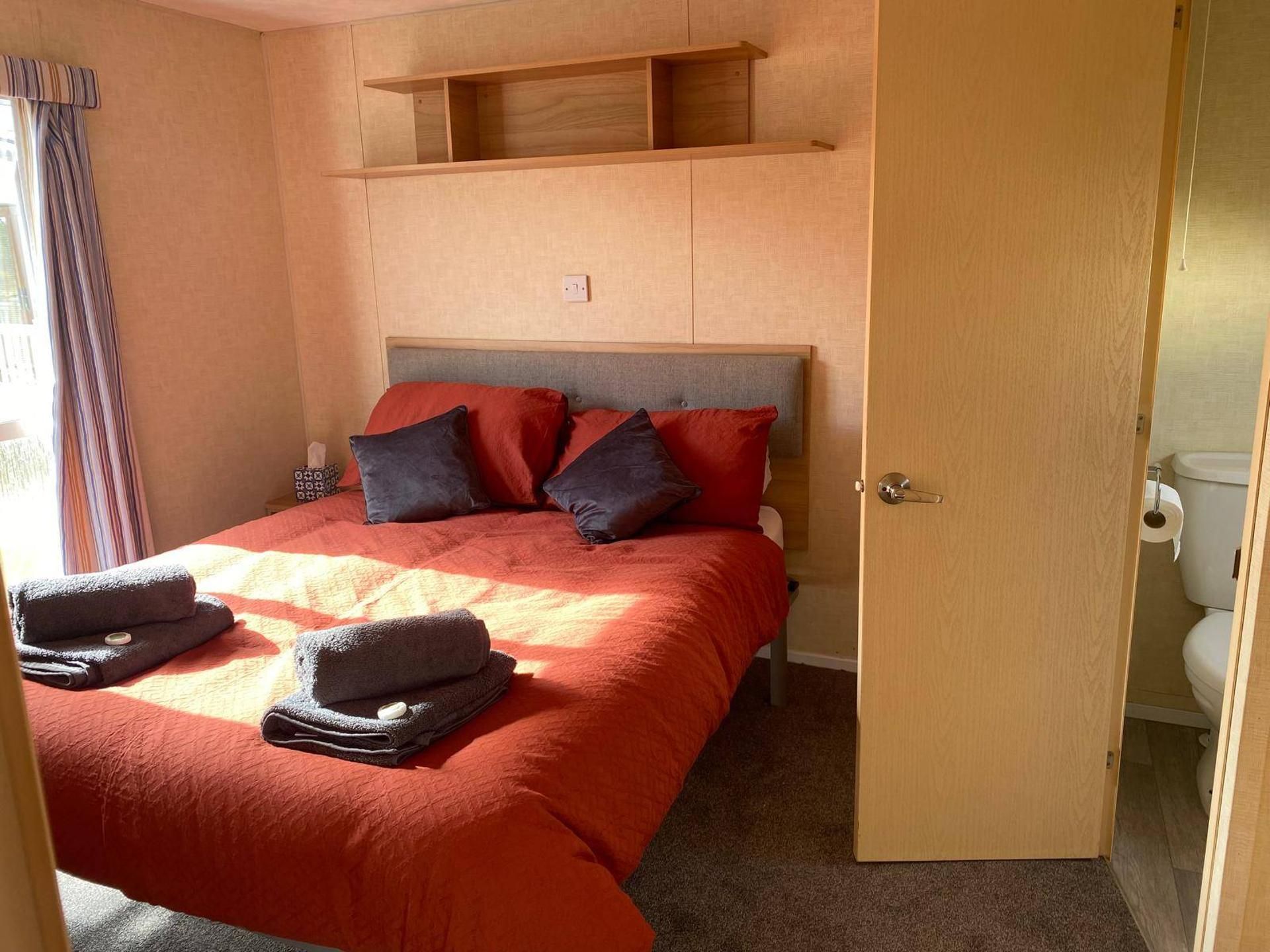 A hotel room with a bed, a wooden headboard, a door, and a bathroom visible through an open door.