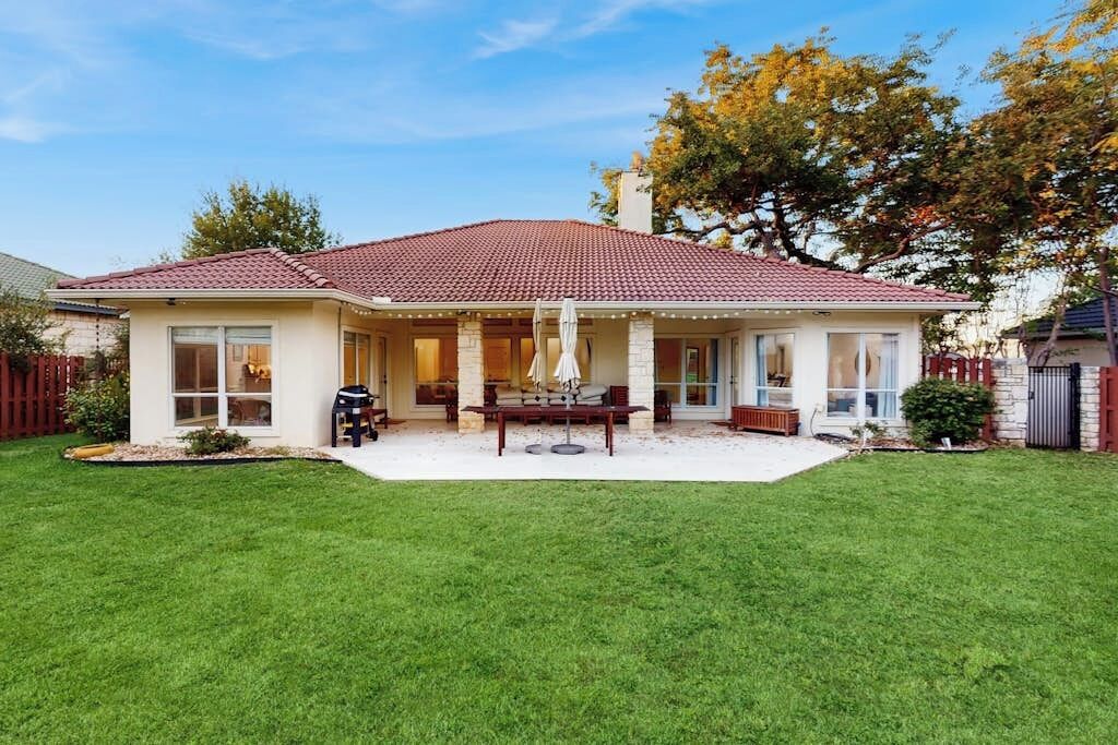 A two-story house with a covered patio, a lawn, and a tree.