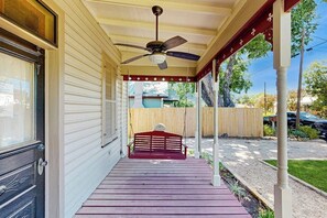 Eine Veranda mit einer roten Bank, einem Deckenventilator und einem Holzzaun im Hintergrund.