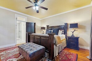 Ein Schlafzimmer mit einem Bett, einer Kommode, einem Nachttisch, einer Lampe, einem Deckenventilator und einem gemusterten Teppich.