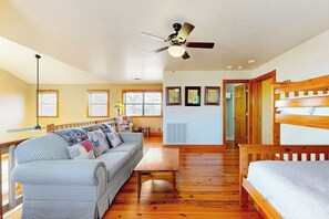 A room with a wooden floor, a sofa, a bed, a ceiling fan, and framed pictures on the wall. - Peaceful Home With Fire Pit, Gazebo, Patio, & Amazing Deck Views - Dog-friendly (Fredericksburg)