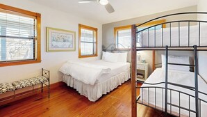 Un dormitorio con una cama individual, una litera, una mesita de noche, una silla y un ventilador de techo.