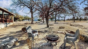 Un área de estar al aire libre con sillas y una parrilla, rodeada de árboles y un edificio.