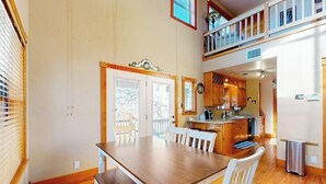 Un comedor con mesa y sillas de madera, una cocina con armarios de madera, y un balcón con barandilla.
