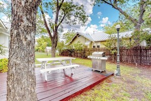 Ein Garten mit einer Holzterrasse, einem Grill und einem Picknicktisch.