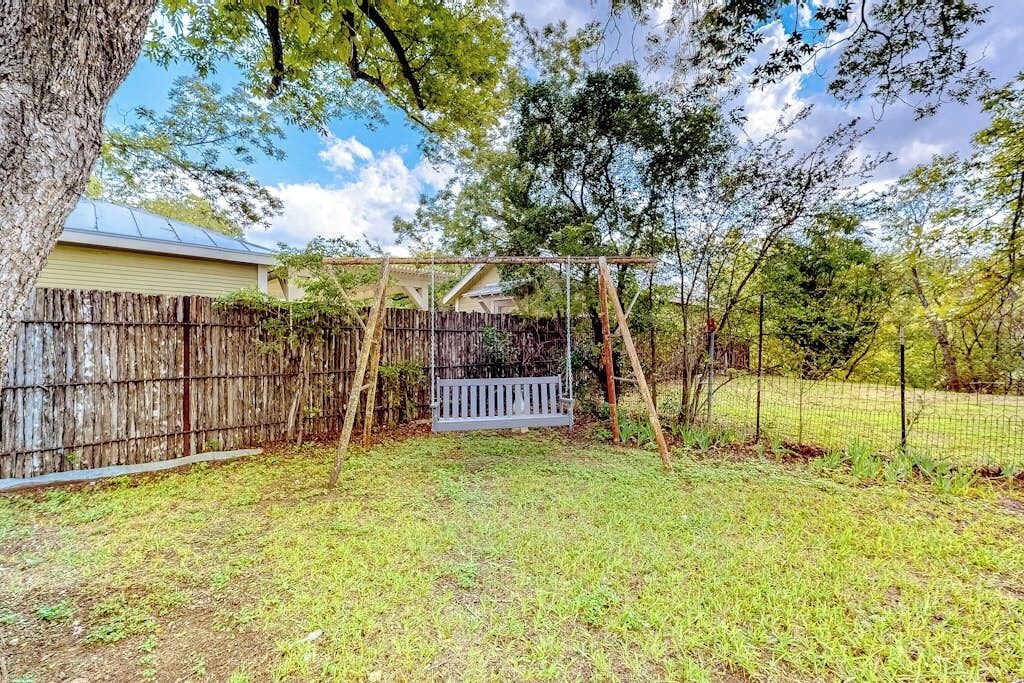 A backyard with a wooden swing set, a wooden fence, and a house in the background.
