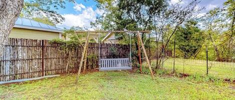 A backyard with a wooden swing set, a wooden fence, and a house in the background.