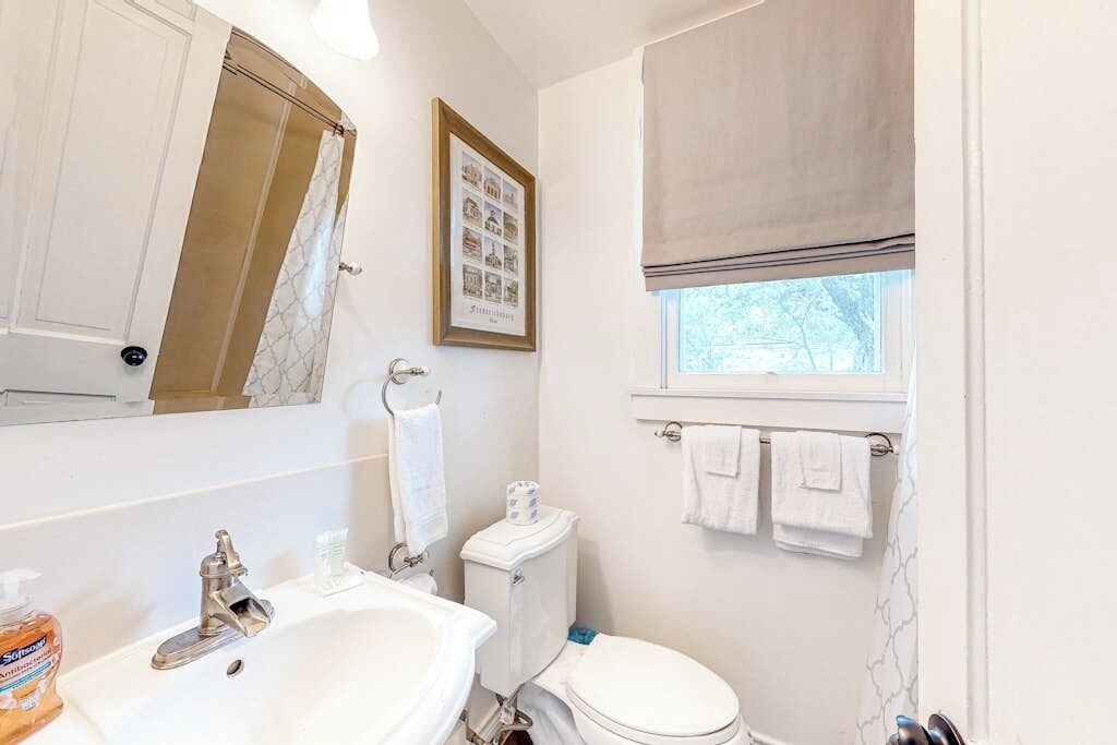 Un baño con lavamanos, inodoro y ventana, con un perchero para toallas.