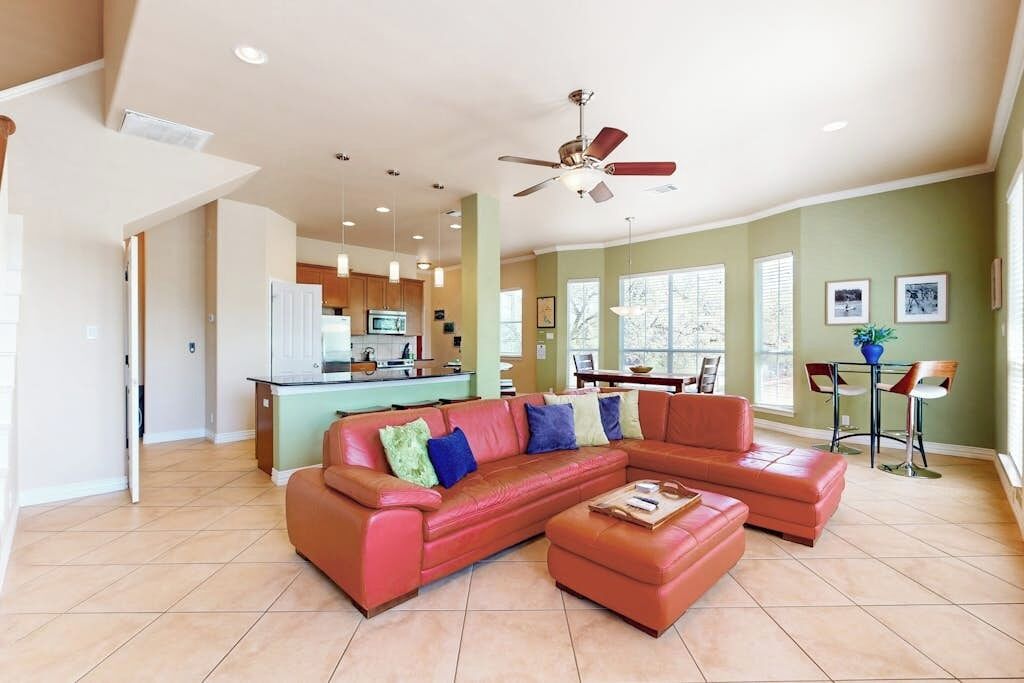 A spacious living room with a sectional sofa, a ceiling fan, and a kitchen in the background.