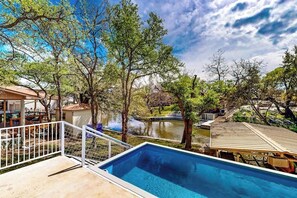 Piscina com vista para um lago, rodeada por árvores e um edifício com telhado.