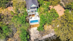 A two-story house with a swimming pool, surrounded by dense trees and a rocky landscape. - Waterfront Home With Game Room, Decks, Pool, Smart Tvs, Kayaks, & Gas Grill (Kingsland)