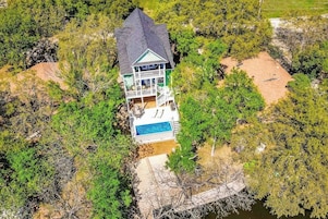 Una casa de dos pisos con piscina, rodeada de árboles frondosos y un paisaje rocoso.
