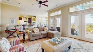 A spacious living room with a sectional sofa, a striped armchair, a coffee table, and a ceiling fan. - Sacred Vista Opulent Hill Country Gem Amazing Patio & Great View (Horseshoe Bay)