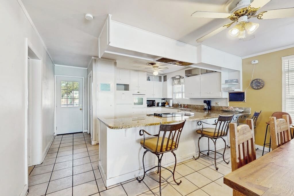 A kitchen with a central island, bar stools, a ceiling fan, and a dining table with chairs.