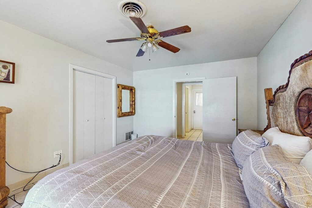 Une chambre à coucher avec un lit, un ventilateur de plafond, une tête de lit en bois et une porte donnant sur une autre pièce.