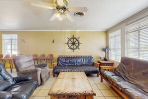 Un salon doté d’un ventilateur de plafond, d’une table basse en bois, de canapés en cuir et d’un gouvernail de bateau fixé au mur.