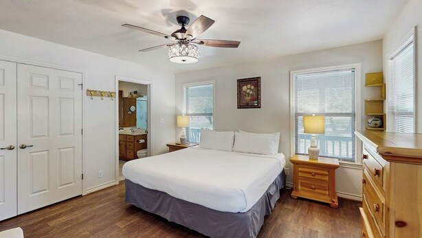 A bedroom with a bed, a ceiling fan, a nightstand with a lamp, a dresser, and a window with blinds. - Idyllic Home With Firepit, Gazebo, Patio, & Amazing Deck Views - Dog-friendly (Fredericksburg)