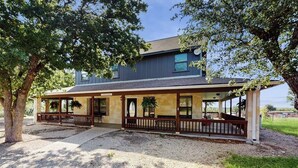 A two-story house with a covered porch, a driveway, and a large tree. - Idyllic Home With Firepit, Gazebo, Patio, & Amazing Deck Views - Dog-friendly (Fredericksburg)