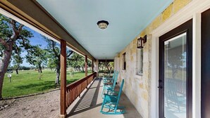 A covered porch with chairs, a door with a window, and a stone wall. - Idyllic Home With Firepit, Gazebo, Patio, & Amazing Deck Views - Dog-friendly (Fredericksburg)