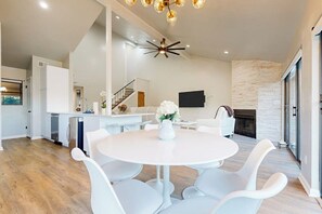 A modern kitchen with white cabinets, a dining area with a round table and white chairs, a staircase, and a fireplace. - Dog-friendly Waterfront Retreat With a Washer/dryer, Furnished Patio, & AC (Horseshoe Bay)