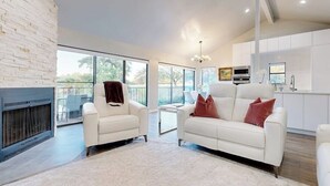 A modern living room with a fireplace, white sofas, and a kitchen in the background. - Dog-friendly Waterfront Retreat With a Washer/dryer, Furnished Patio, & AC (Horseshoe Bay)