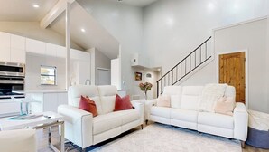 A modern living room with white sofas, a coffee table, and a staircase leading to an upper level. - Dog-friendly Waterfront Retreat With a Washer/dryer, Furnished Patio, & AC (Horseshoe Bay)