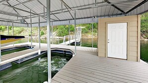 A covered outdoor swimming area with a wooden deck, a dock, and a white door. - Natural Cliffside Oasis With Impressive Views, Gas Fireplace and Dock (Spicewood)
