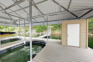 A covered outdoor swimming area with a wooden deck, a dock, and a white door. - Natural Cliffside Oasis With Impressive Views, Gas Fireplace and Dock (Spicewood)