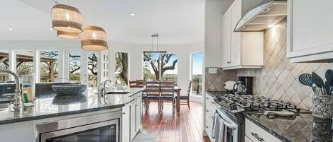 A modern kitchen with a central island, stainless steel appliances, and a dining area with a view.