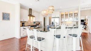 A modern kitchen with white cabinetry, a central island with bar stools, pendant lighting, and a stainless steel range hood. - Natural Cliffside Oasis With Impressive Views, Gas Fireplace and Dock (Spicewood)