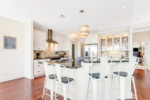 A modern kitchen with white cabinetry, a central island with bar stools, pendant lighting, and a stainless steel range hood. - Natural Cliffside Oasis With Impressive Views, Gas Fireplace and Dock (Spicewood)
