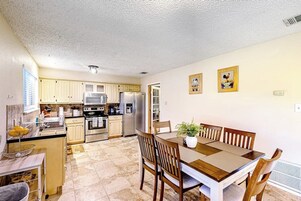 Una cocina con comedor, que incluye armarios, un refrigerador, un microondas y una mesa de comedor con sillas.